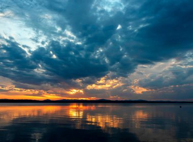 Gölün üzerinde çok renkli mavi ve turuncu günbatımı gökyüzü, bulutların fantastik bir resmi, sakin suyun yansımaları, güney Urallar, Uvildy Gölü
