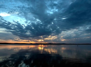 Gölün üzerinde çok renkli mavi ve turuncu günbatımı gökyüzü, bulutların fantastik bir resmi, sakin suyun yansımaları, güney Urallar, Uvildy Gölü