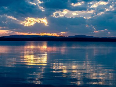 Gölün üzerinde çok renkli mavi ve turuncu günbatımı gökyüzü, bulutların fantastik bir resmi, sakin suyun yansımaları, güney Urallar, Uvildy Gölü