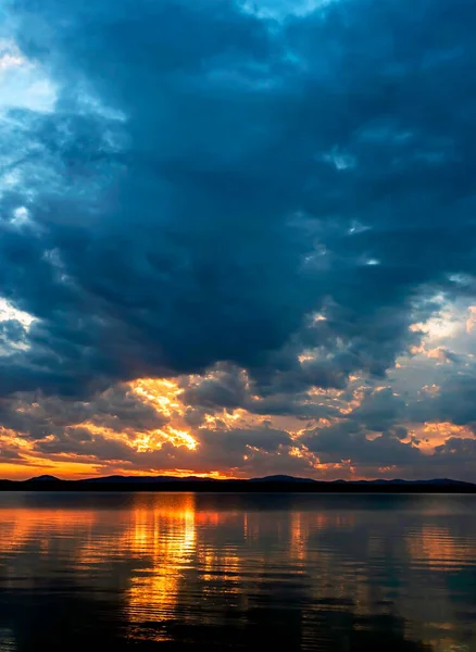 dark evening sky over the lake, dramatic clouds, the light of the sun is still visible, reflections on the water, summer evening, Southern Urals, Lake Uvildy