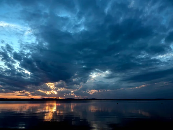 dark evening sky over the lake, dramatic clouds, the light of the sun is still visible, reflections on the water, summer evening, Southern Urals, Lake Uvildy