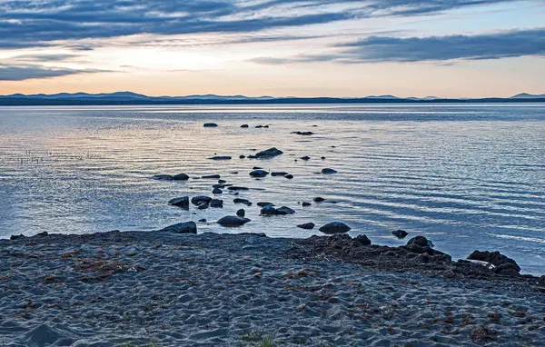 호수의 저녁해 지평선 아래로 있습니다 해변에서 호수로 돌들이 들어가고 있습니다 — 스톡 사진