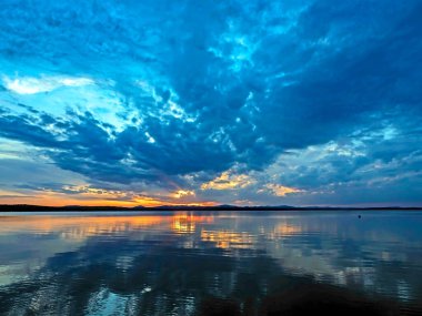 Gölün üzerinde çok renkli mavi ve turuncu günbatımı gökyüzü, bulutların fantastik bir resmi, sakin suyun yansımaları, güney Urallar, Uvildy Gölü