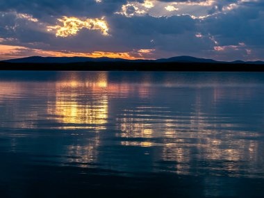 Gölün üzerinde çok renkli mavi ve turuncu günbatımı gökyüzü, bulutların fantastik bir resmi, sakin suyun yansımaları, güney Urallar, Uvildy Gölü
