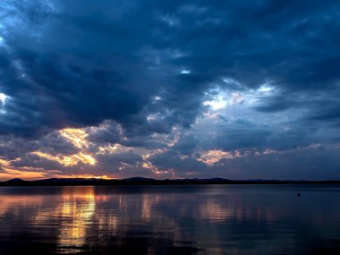 Gölün üzerinde karanlık akşam gökyüzü, dramatik bulutlar, güneşin ışığı hala görünür, suda yansımalar, yaz akşamı, Güney Uviller, Uvildy Gölü