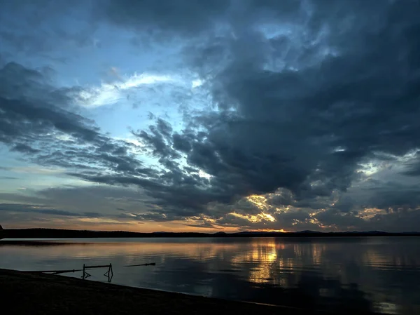 dark evening sky over the lake, dramatic clouds, the light of the sun is still visible, reflections on the water, summer evening, Southern Urals, Lake Uvildy