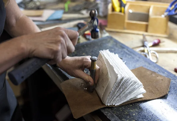 Bookbinder hammers hardware to back of custom book. — Stock Photo, Image