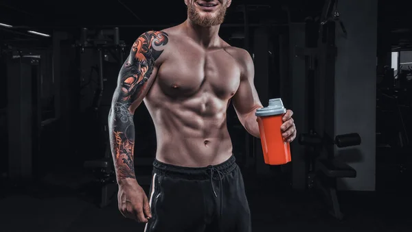 Portrait of an athlete standing with a shaker in the gym. Bodybuilding and fitness concept. Mixed media