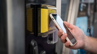 Akıllı telefon tutan ve elektronik terminalde cep telefonu taksiti ödemeyen birinin yakın çekimi. Modern NFC kablosuz teknoloji, güvenli dijital işlemler, nakitsiz sistem ve kullanışlı