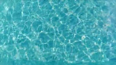 Berrak mavi suyun yüzeyi sürekli dalgalanmaları ve yansımaları ortaya çıkarır, suyun yüzeyinde parıldayan ışığın hareketini ve etkileşimini yakalar.
