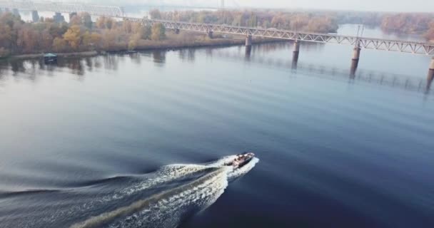 Переліт безпілотного літального апарата над човном на річці восени вкритий туманом, на тлі міста Києва. — стокове відео