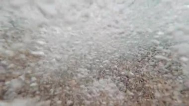 Dalgalar sırasında suyun altında bir manzara, bir sürü baloncuk ve kum, yakın çekim.