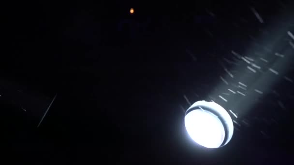 Концертные прожекторы ночью во время снегопада, снежинки, вращающиеся на свет — стоковое видео