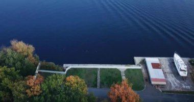 Üzerinde çim ve yat olan bir plaj. Adayı sonbahar ağaçlarıyla gören bir manzarayla..