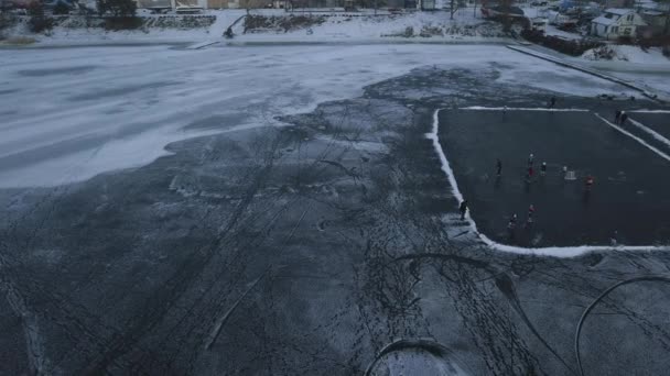 Vuelo en avión no tripulado sobre un lago congelado donde los niños entrenan y juegan hockey cerca de la orilla en un día nublado — Vídeos de Stock