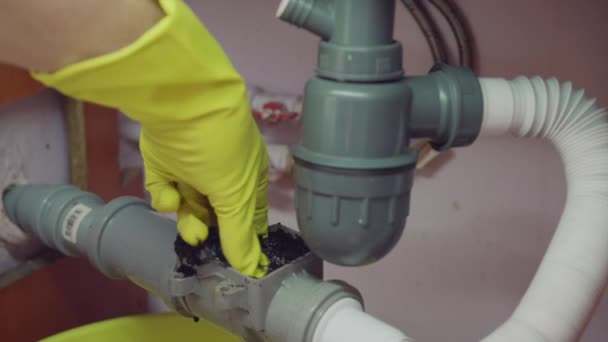 Clearing a blockage in the plumbing check valve in the kitchen, A hand in a yellow glove takes out the trash. — 비디오