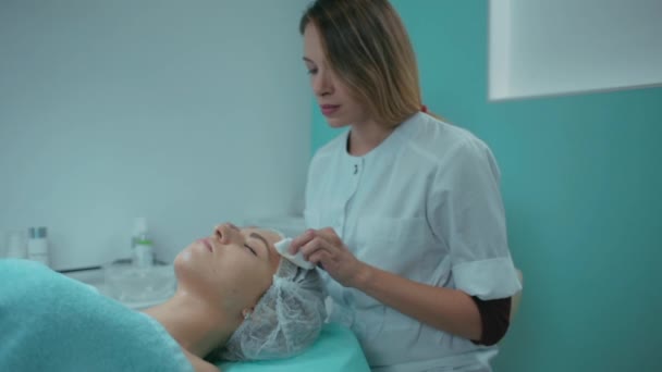 Уборка лица девушки перед процедурой косметолога в офисе — стоковое видео