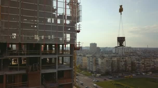 Élévation d'une citerne avec du béton sur le toit d'un immeuble de grande hauteur en construction avec des travailleurs portant des casques dans le contexte de la vie urbaine, dans le rétroéclairage — Video