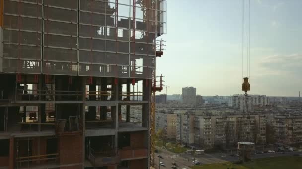 Подъем цистерны с бетоном на крыше строящегося высотного здания с рабочими в шлемах на фоне городской жизни, в подсветке — стоковое видео