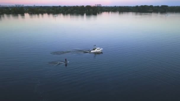 Ο αθλητής σηκώνεται από το νερό και κάνει foilboarding κρατώντας το σχοινί δεμένο στο σκάφος στη βραδινή εναέρια θέα — Αρχείο Βίντεο