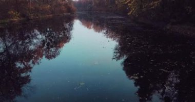 Sonbahar ağaçlarının manzarası ve renkli yaprakların yansımaları ile nehir üzerinde uçan kamera.