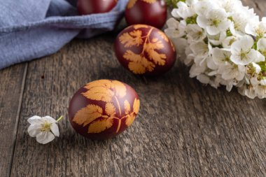 Paskalya yumurtaları soğan kabuklarıyla boyanmış. Masada bitkiler ve arka planda kiraz çiçekleri var.