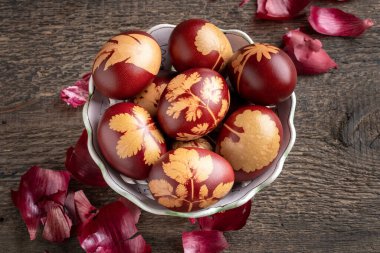 Paskalya yumurtaları soğan kabuklarıyla boyanmış. Beyaz bir kasede çeşitli bitkiler var.