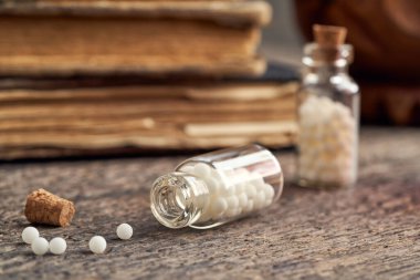 Arka planda antika kitaplar olan, ahşap bir arka planda bir şişe homeopatik hap.