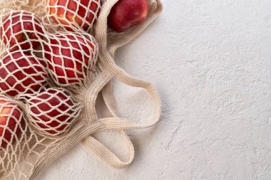 Organik pamuktan yapılmış, yeniden kullanılabilir ekolojik bir ağ torbasında taze elmalar, fotokopi alanı ile parlak bir arka planda.