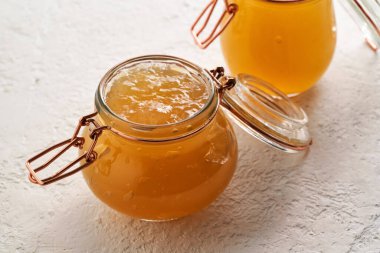 Beyaz arka planda iki cam kavanozda soğumuş et suyu çorbası.