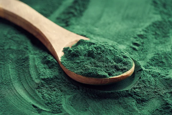 Yeşil arka planda kaşıkta taze spirulina tozu.