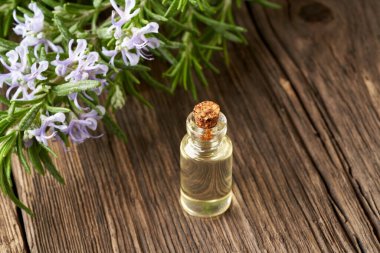 Arka planda çiçek açan biberiye dallarıyla birlikte gerekli yağ şişesi.