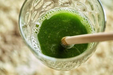 Bir bardağın dibinde, içinde bambu kamışı olan yeşil meyve suyu.