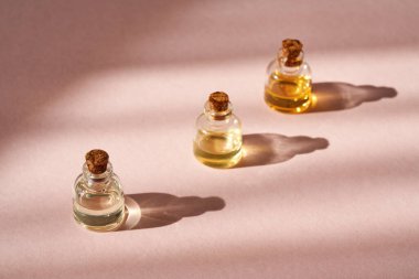 Pembe arka planda gölgeli üç şişe temel yağ.