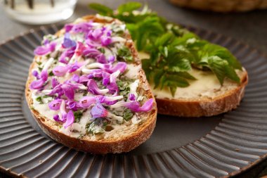 Yaban yenilebilir bahar bitkileriyle bir dilim ekşi ekmek - toprak yaprağı, akciğer otu ve mor ölü ısırgan otu çiçekleri