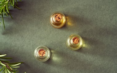 Esaslı yağ şişeleri koyu yeşil arka planda taze biberiye dalları ile