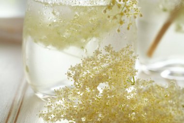 Arka planda bir bardak ev yapımı bitkisel limonata ile taze yaşlı çiçekler.