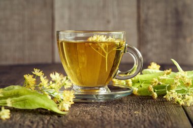 Masada ıhlamur çiçekleri olan bir fincan bitki çayı. Öksürük ve soğuğa karşı alternatif ilaç..