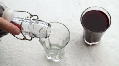 Pouring homemade black elder syrup from a bottle into a glass