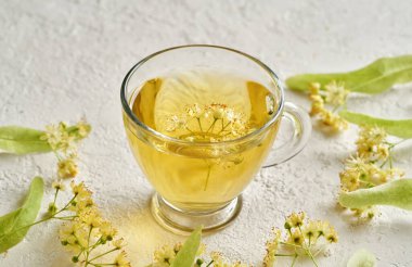 Beyaz arka planda taze ıhlamur çiçekleri olan bir fincan bitki çayı.