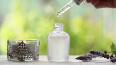 Aromaterapi damlaları, bir mum ve taze nane çiçekleriyle şişeye dökülen gerekli yağ damlaları.