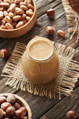 Ahşap bir masada cam kavanozda ev yapımı fındık ezmesi.