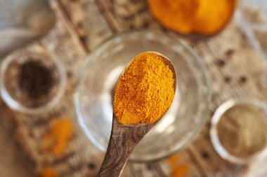 Kuru zerdeçal kökü tozu bir bardak suyun üzerinde tahta bir kaşık üzerinde, zemin ve arka planda tüm siyah biber ile. Üst görünüm.