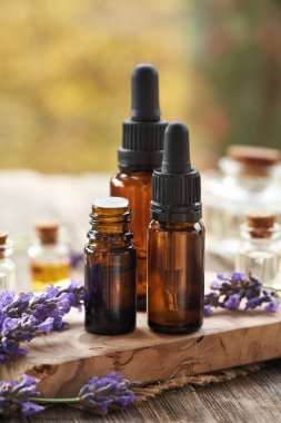 Sonbaharda açık bir masada taze lavanta çiçekleriyle üç kahverengi yağ şişesi.