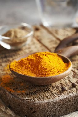 Ahşap bir kaşıkta zerdeçal kökü tozu ve arka planda da karabiber.