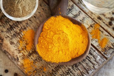 Bir kaşık dolusu kuru zerdeçal kökü tozu zemin ve tüm siyah biber, üst manzara.