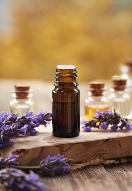 Açık bir masada üzerinde taze çiçek açan lavanta bitkisi olan koyu renkli bir yağ şişesi.
