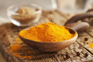 Kuru zerdeçal kökü tozu ve arka planda kara biber.