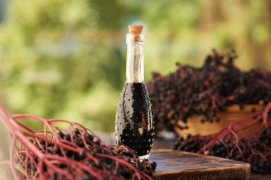 Bir şişe siyah yaşlı şurubu ve açık bir masada taze elderberry.