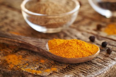 Bir kaşıkta zerdeçal kökü tozu ve arka planda da tüm siyah biber.